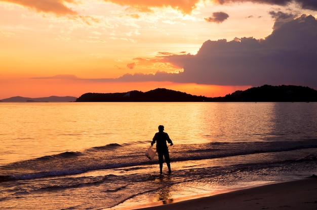 Silueta de hombre solitario caminando hacia el mar al atardecer