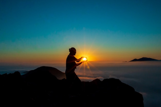 silueta de un hombre tocando el sol con ambas manos en la cima de una montaña