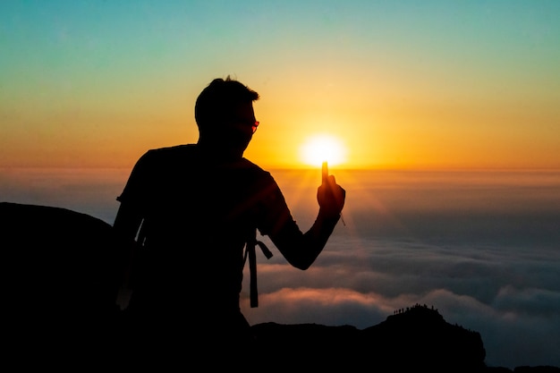 silueta de un hombre tocando el sol con un dedo en la cima de una montaña