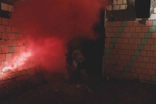 Silueta de un hombre de uniforme con un arma en un antiguo corredor de humo rojo