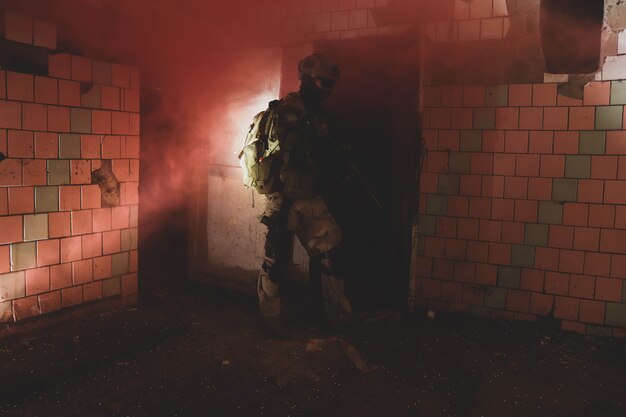 Silueta de un hombre de uniforme con un arma en un antiguo corredor de humo rojo