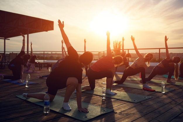 Silueta de hombres y mujeres haciendo yoga al aire libre en el techo al atardecer