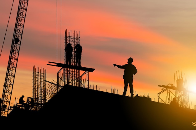 Silueta de ingeniero y trabajador en el sitio de construcción del sitio de construcción al atardecer por la noche