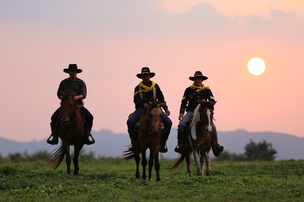 La silueta del jinete como traje de vaquero con un caballo y una pistola en la mano contra el humo y el fondo del atardecer