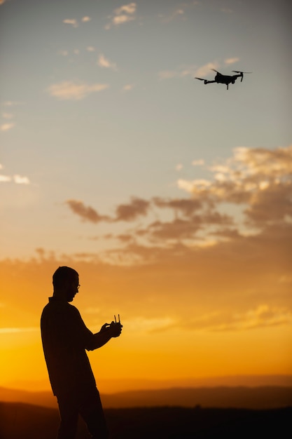 Silueta de un joven operando un dron en un entorno rural al atardecer