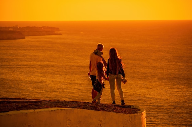 Silueta de una joven pareja romántica con un niño disfrutando de la noche en un acantilado sobre el mar