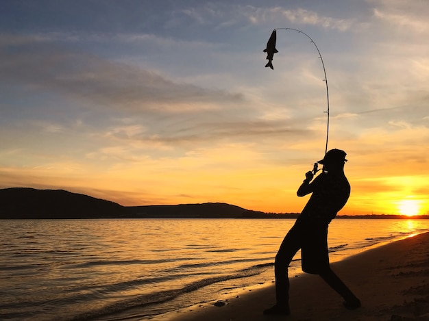 Silueta de joven pescando en el lago al atardecer