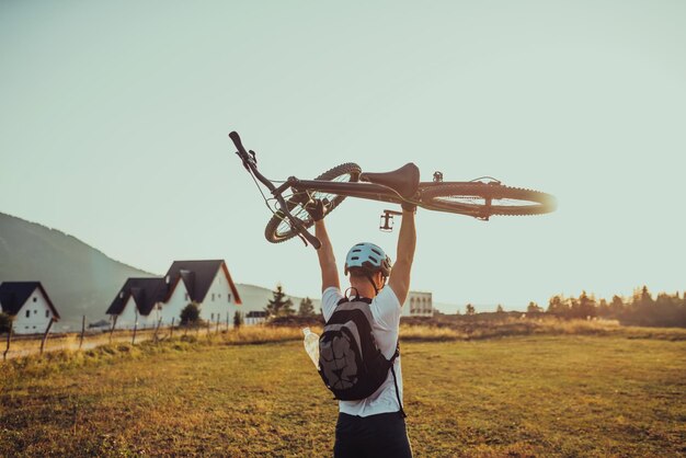 Silueta de un joven sosteniendo una bicicleta en el campo al atardecer con un cielo dramático en el fondo Foto de alta calidad