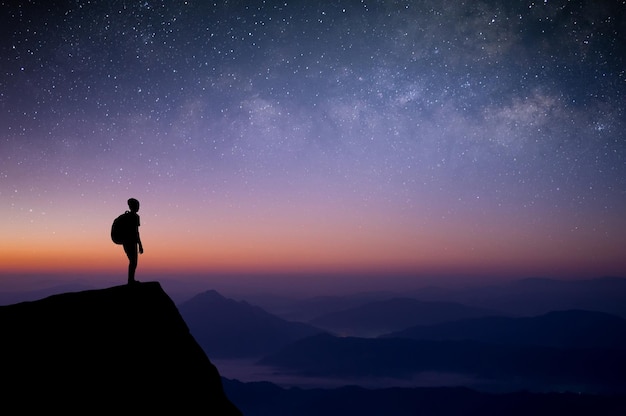 Silueta de joven viajero con mochila de pie y vio la estrella vía láctea y el cielo nocturno solo en la cima de la montaña Disfrutó viajar y tuvo éxito cuando llegó a la cima