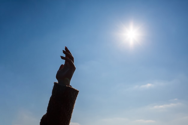 La silueta de una mano femenina contra un cielo azul y un sol brillante