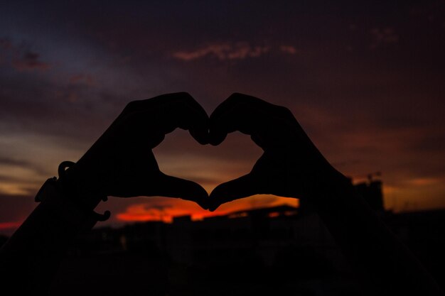 Foto silueta de mano en forma de corazón en el fondo del atardecer