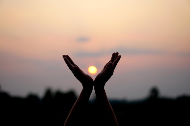 Silueta de mano humana levantada para pedir un deseo fondo de puesta de sol