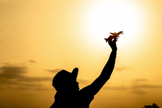 Silueta de la mano que sostiene el modelo de avión en cielo colorido dramático al atardecer