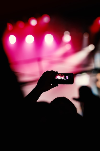 Silueta de manos usando teléfonos inteligentes para tomar fotos y videos en el show de música en vivo.