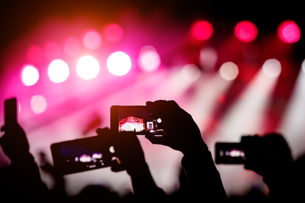 Silueta de manos usando teléfonos inteligentes para tomar fotos y videos en el show de música en vivo.