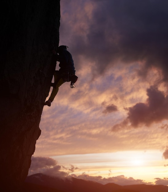 Silueta masculina escalada en roca haciendo el siguiente paso en el acantilado Cielo nublado púrpura oscuro en el fondo con espacio de copia Ángulo bajo