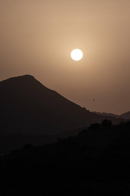 Silueta de montañas mientras cae el atardecer con el sol de fondo a la hora naranja