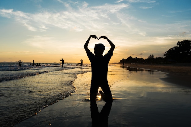 Silueta del muchacho joven que hace la muestra del corazón con sus brazos en la playa
