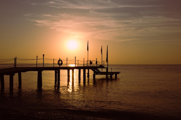 Silueta de un muelle marino de madera contra el fondo del sol naciente