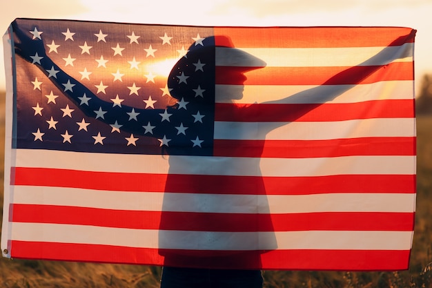 Silueta de mujer al atardecer en el campo agrícola detrás de la bandera americana