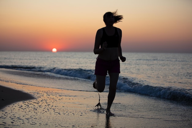 Silueta de una mujer atleta sobre un fondo de amanecer en el mar