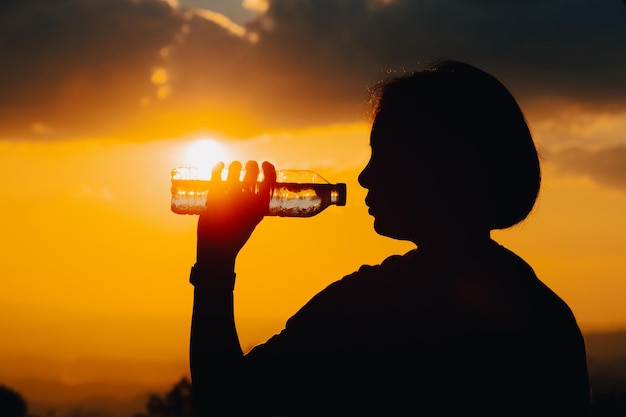 Silueta de una mujer bebiendo agua bebiendo agua al atardecer