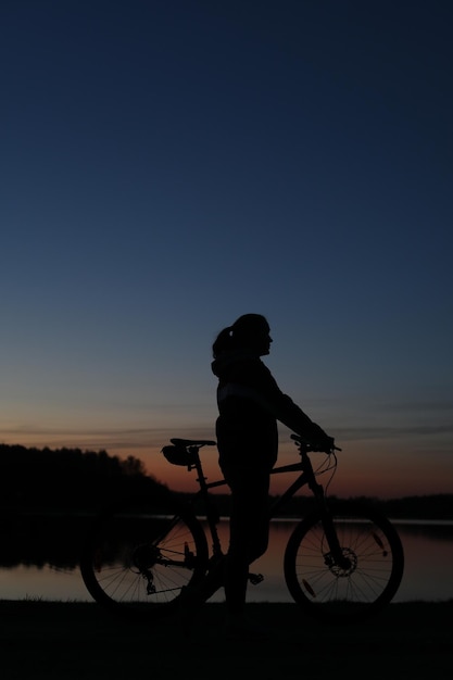 Silueta de mujer con bicicleta de montaña sobre fondo de puesta de sol de cielo azul colorido Estilo de vida activo al aire libre