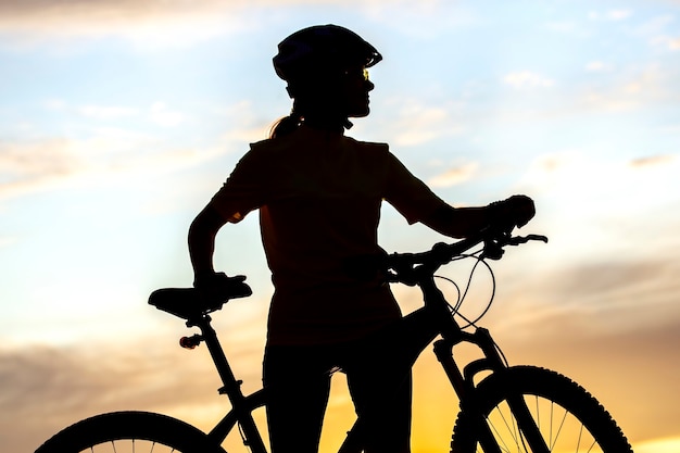 Silueta de una mujer ciclista con una bicicleta en el fondo de un cielo al atardecer. Estilo de vida saludable y deporte. Ocio y aficiones