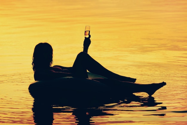 Foto silueta de una mujer con una copa de vino en el agua durante una hermosa puesta de sol