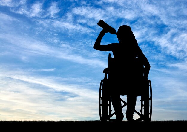 Silueta de una mujer discapacitada en silla de ruedas bebiendo agua de una botella de plástico. Concepto de ocio y recreación para personas con discapacidad