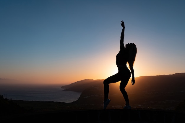 Silueta de mujer disfrutando de la libertad sintiéndose feliz al atardecer con montañas y mar