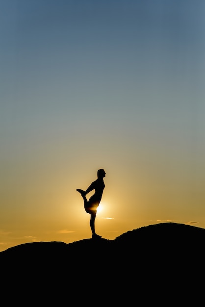 Silueta de mujer haciendo yoga en una puesta de sol