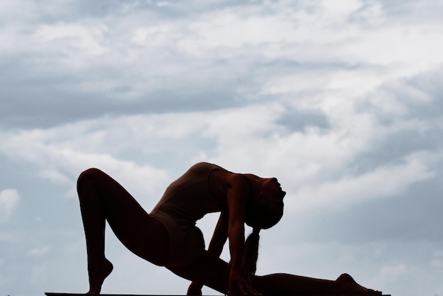 Silueta de mujer hermosa joven en ropa deportiva haciendo estiramientos antes de hacer ejercicio al aire libre en forma bo