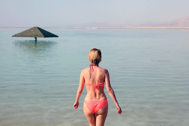 Silueta de una mujer joven caminando por la orilla salada del Mar Muerto al amanecer hacia el sol en Israel