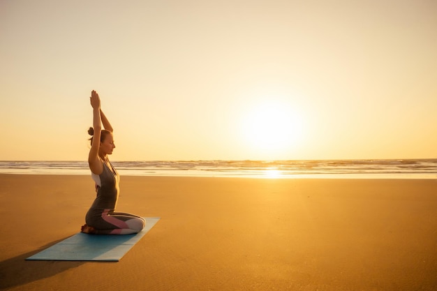 Silueta de mujer joven en un elegante traje de yogui haciendo yoga en la playa en pose copia espacio.