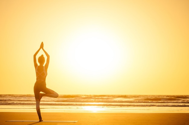 Silueta de mujer joven en un elegante traje de yogui haciendo yoga en la playa en pose copia espacio.