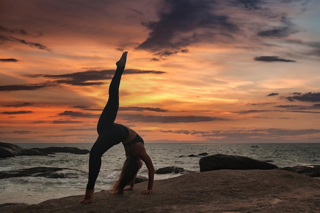 Silueta mujer joven hace divisiones de posición de yoga o cordeles para un estilo de vida saludable en la costa tropical