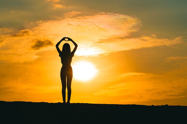 Silueta de mujer joven hace una promesa, la forma del corazón simboliza el amor