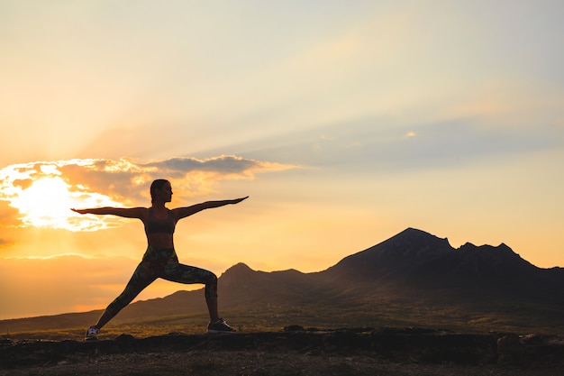 Silueta de mujer joven practicando yoga al atardecer