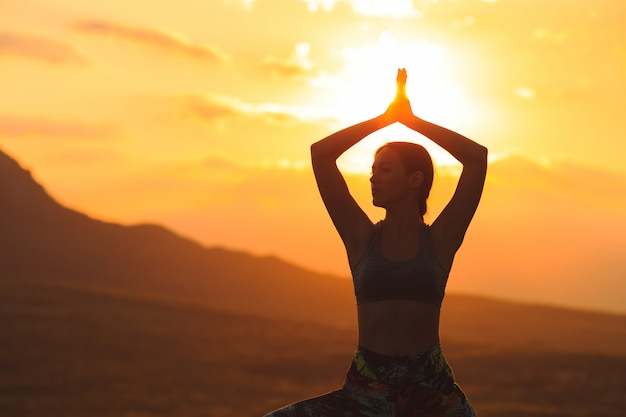 Silueta de mujer joven practicando yoga al atardecer