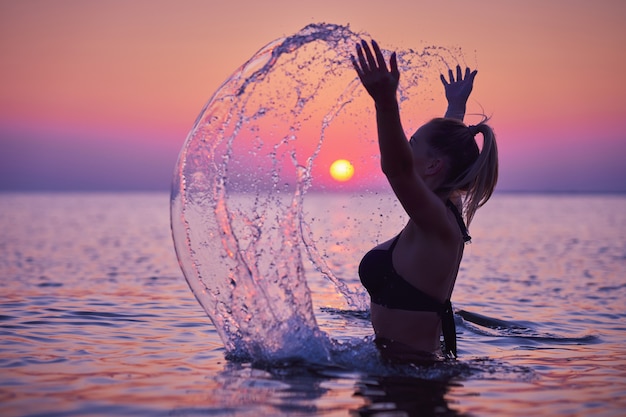 Silueta de mujer joven practicando yoga en la playa al amanecer.