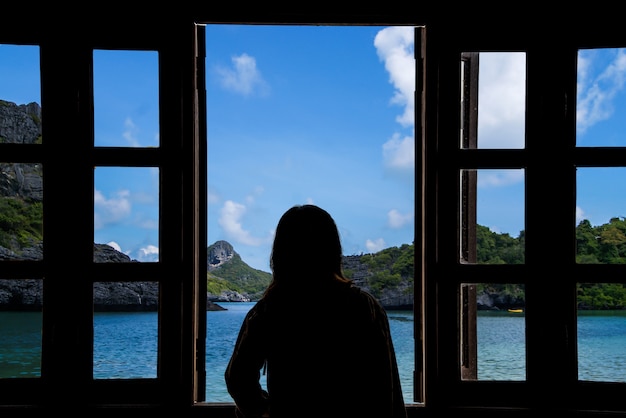 La silueta de una mujer mirando por la ventana con vistas al mar.