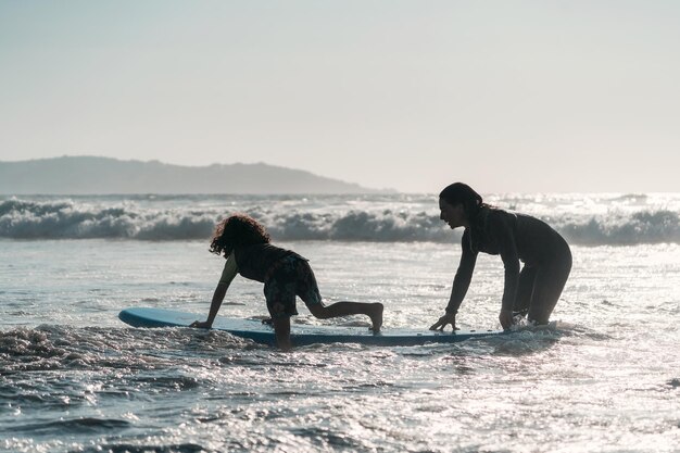 Foto silueta, de, un, mujer, y, niño, con, surfbord, en el agua