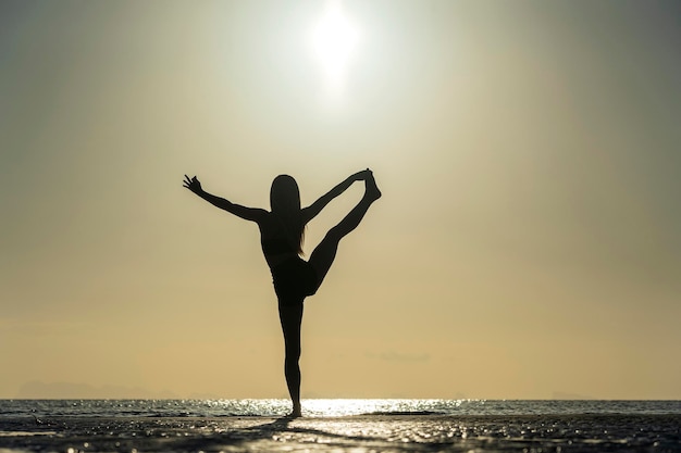 Silueta de mujer de pie en pose de yoga en la playa tropical durante la puesta de sol Chica caucásica practicando yoga cerca del agua de mar