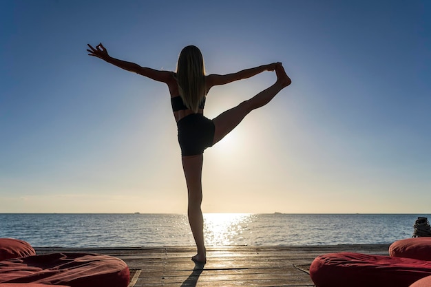 Silueta de mujer de pie en pose de yoga en la playa tropical durante la puesta de sol Chica practicando yoga cerca del agua de mar