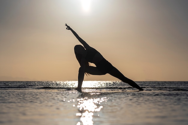 Silueta de mujer de pie en pose de yoga en la playa tropical durante la puesta de sol