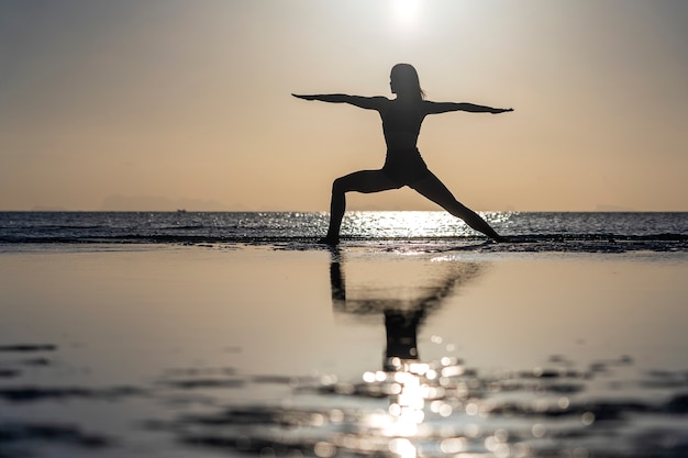 Silueta de mujer de pie en pose de yoga en la playa tropical durante la puesta de sol