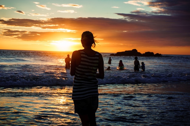 Silueta de mujer en la playa al atardecer, niña caminando sobre la costa del mar en la luz del sol del verano