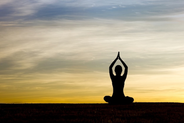 Silueta de mujer practicando yoga al amanecer