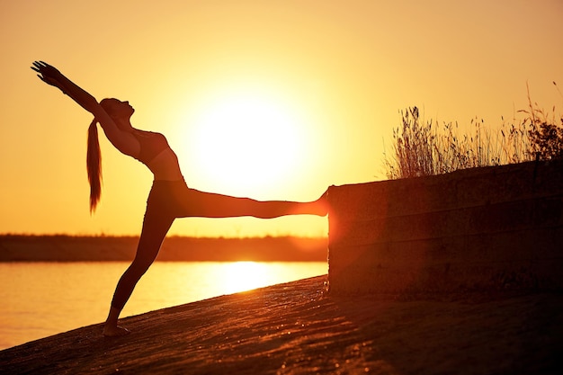 Silueta mujer practicando yoga o estiramientos en el muelle de la playa al atardecer o al amanecer